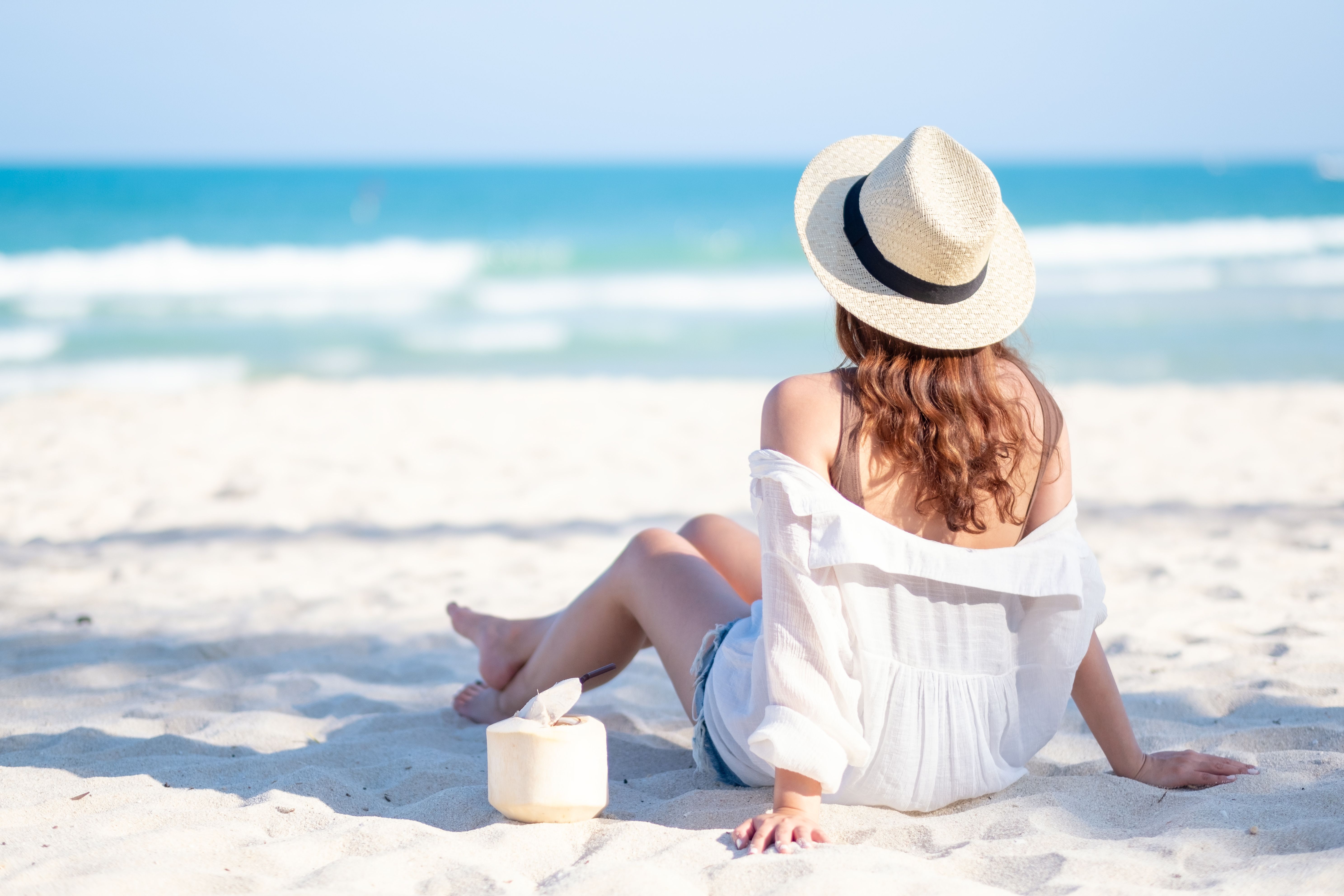 Rear view of a woman sitting on the beach and looking at the sea.