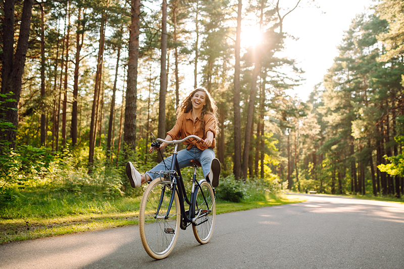 Woman smiling, riding a bike through a park.