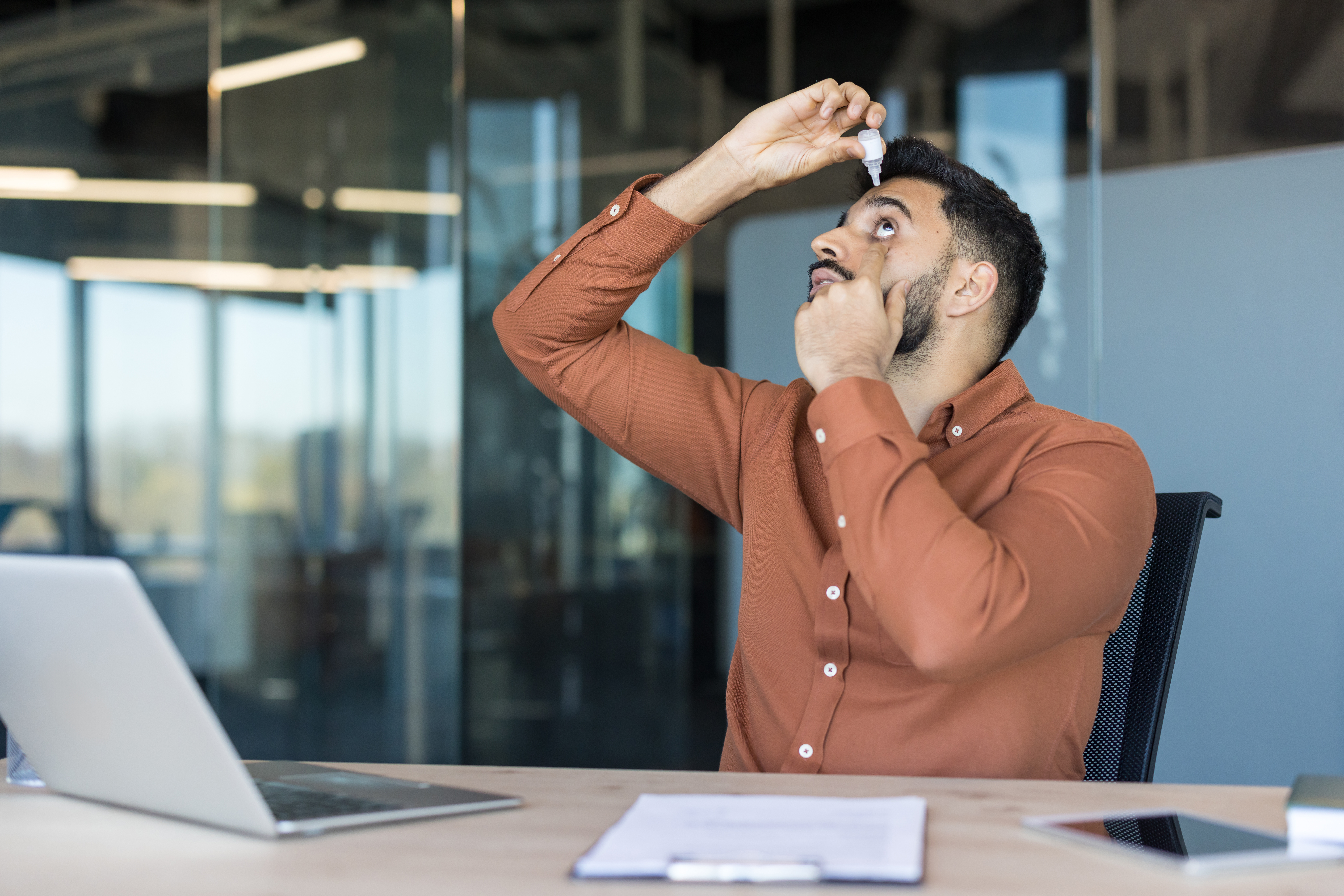 Man in office putting in eye drops.
