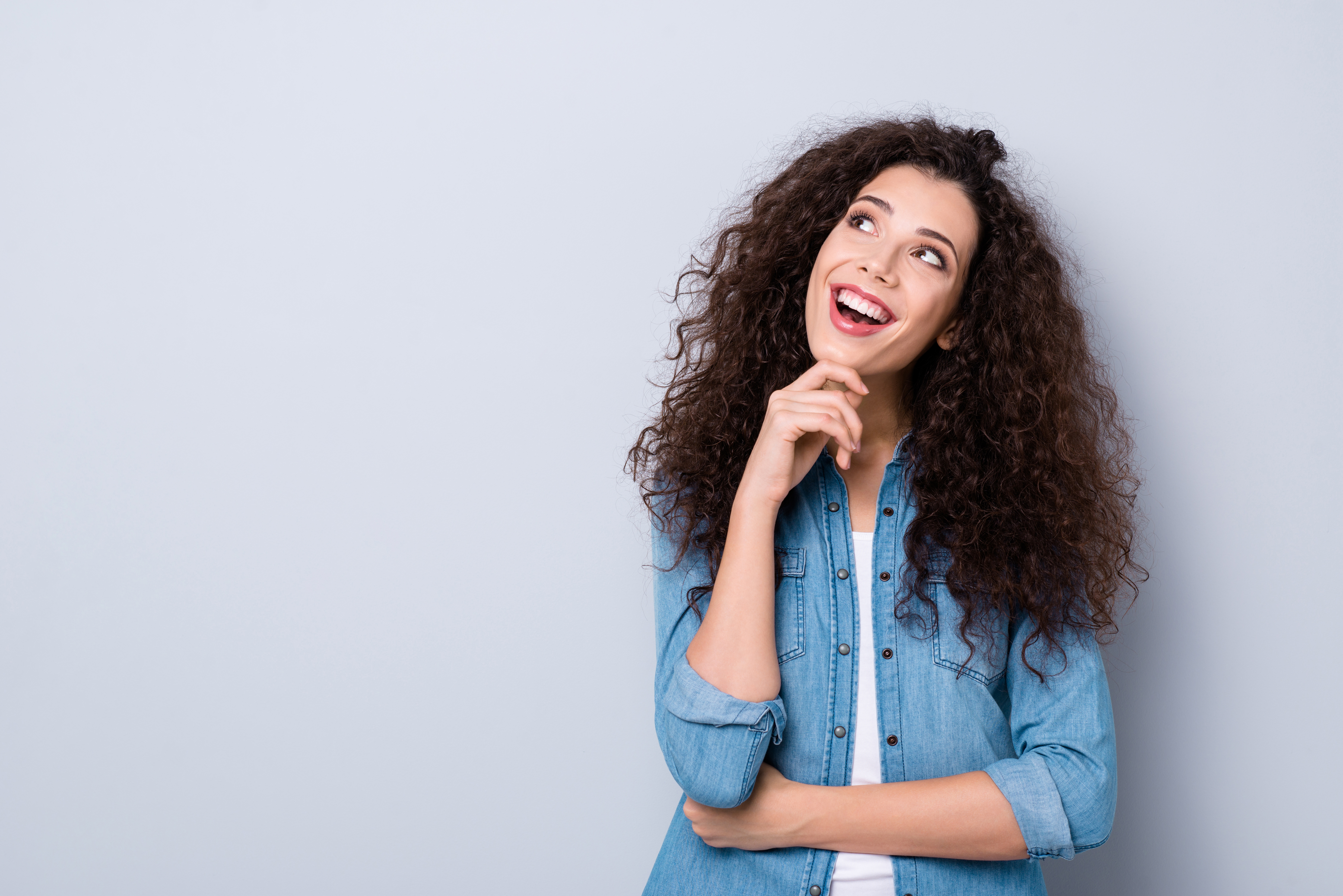 Woman thinking with a smile against a grey background.