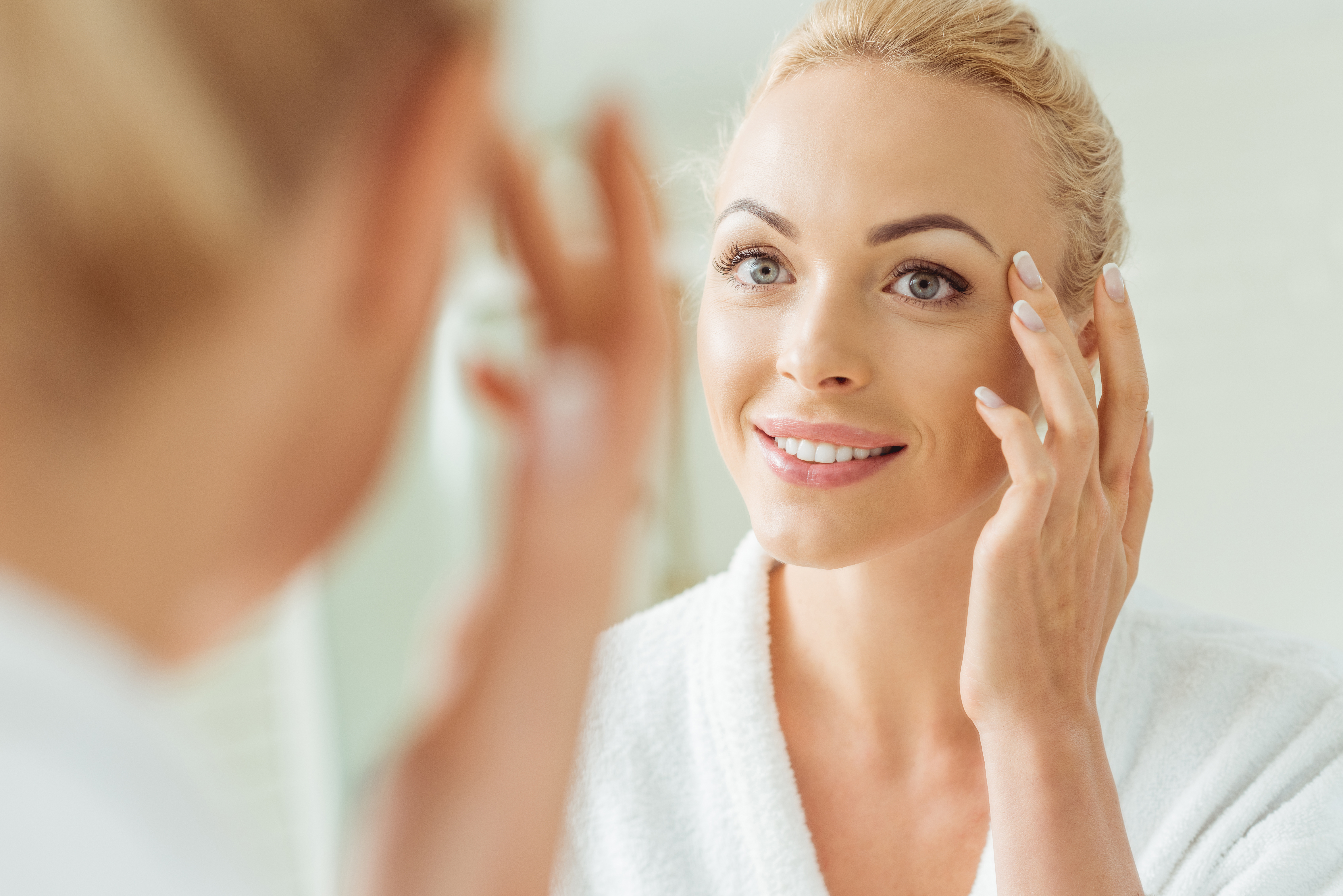 Woman smiling at her reflection in the mirror and admiring her eyes.