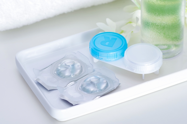 Two contact lenses in their original metal packaging, alongside a white and blue lens case