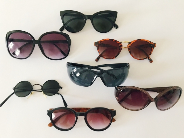 7 pairs of sunglasses of varying sizes and designs on a cream background