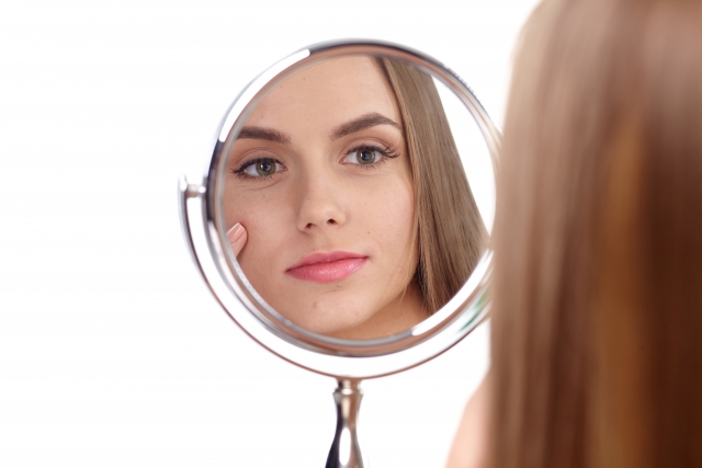 Woman looking at her face in the reflection of a circular mirror