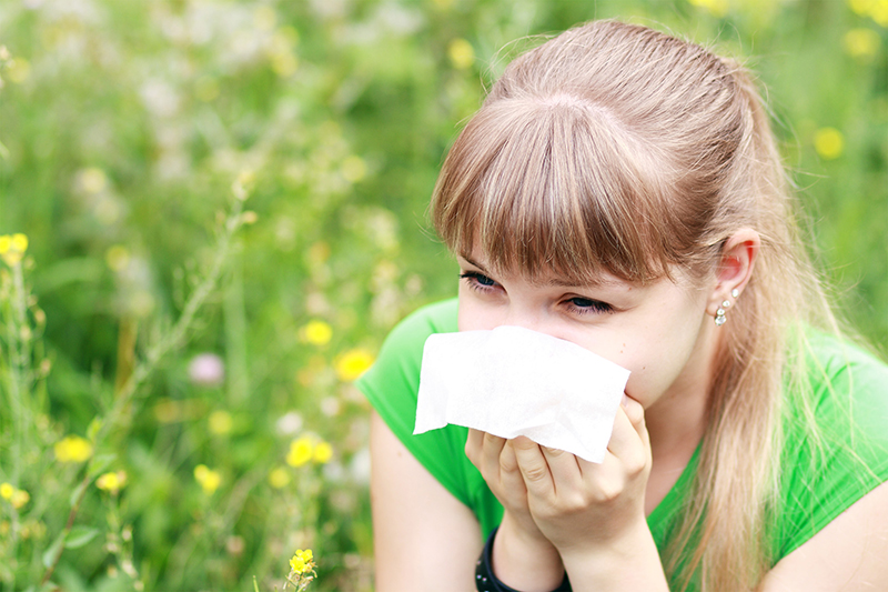 Medium closeup shot of women sitting in meadow sneezing into tissue